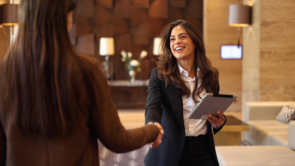 Two professional women in warm conversation in a bright lobby, the welcoming face of the volunteer community