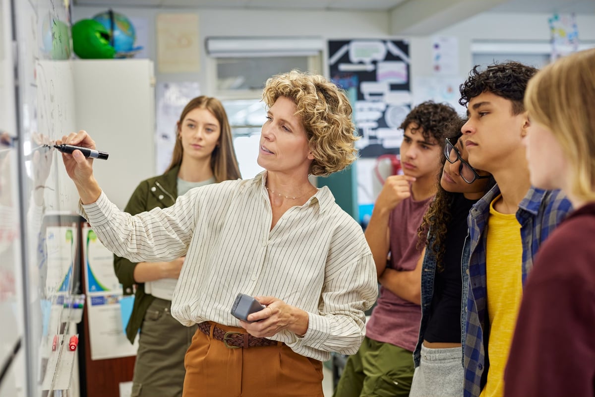 A woman professor teaching a small class of students before a whiteboard, the structured learning of the flagship program