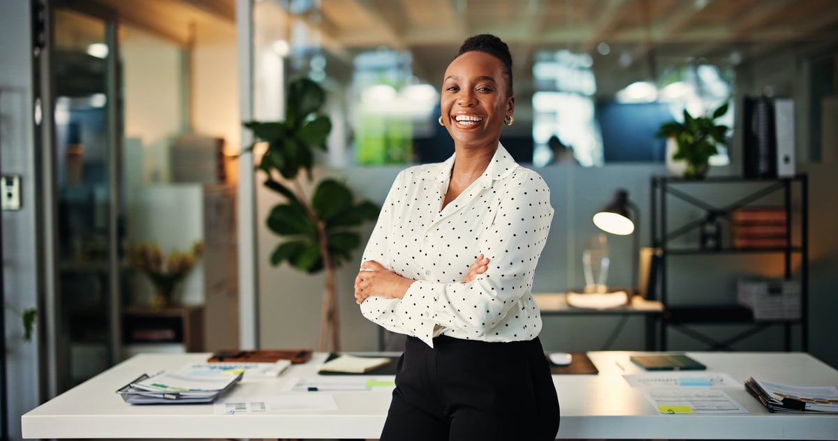 A confident professional woman standing with presence in a modern office, conveying authority and accomplishment