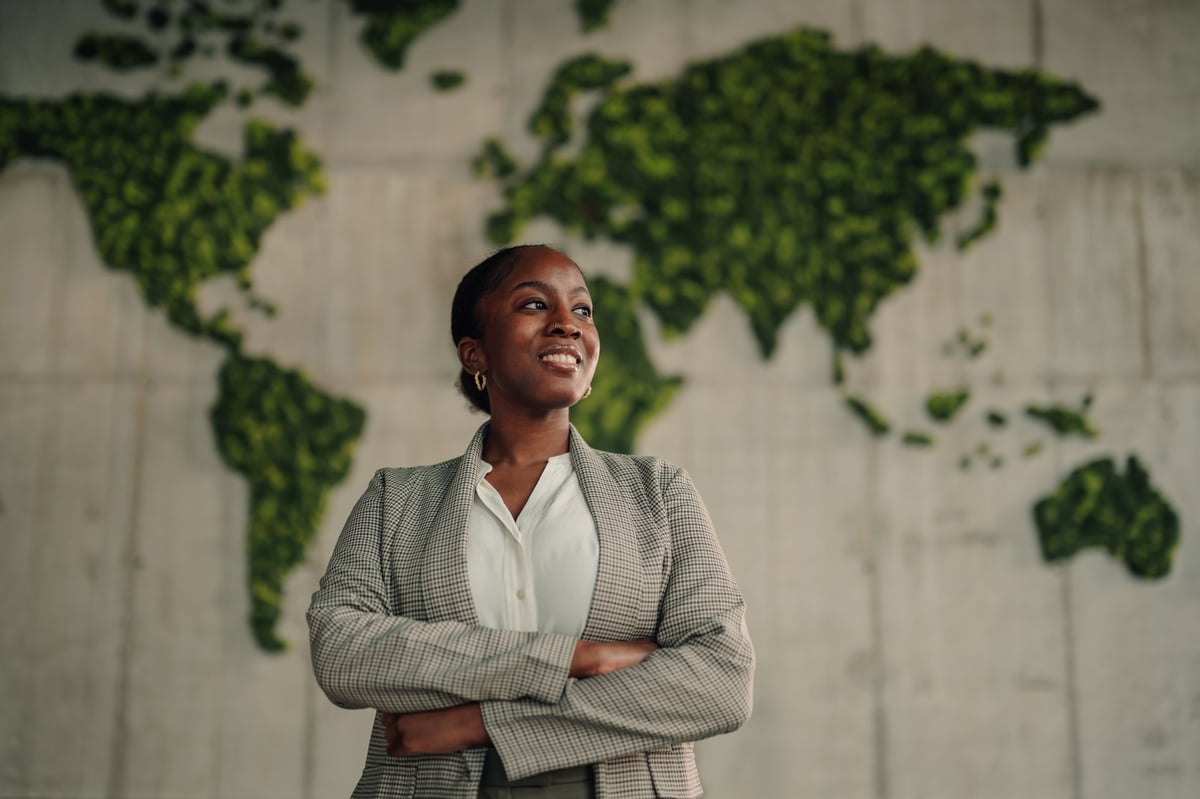 A confident professional woman of presence standing with crossed arms before a world map, a figure of institutional leadership